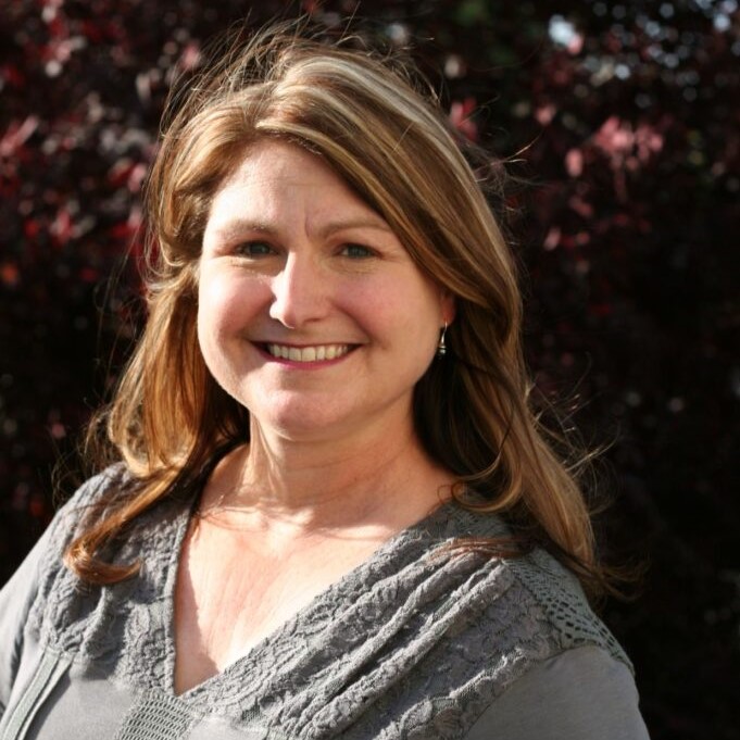 A woman standing in front of a tree smiling for the camera.