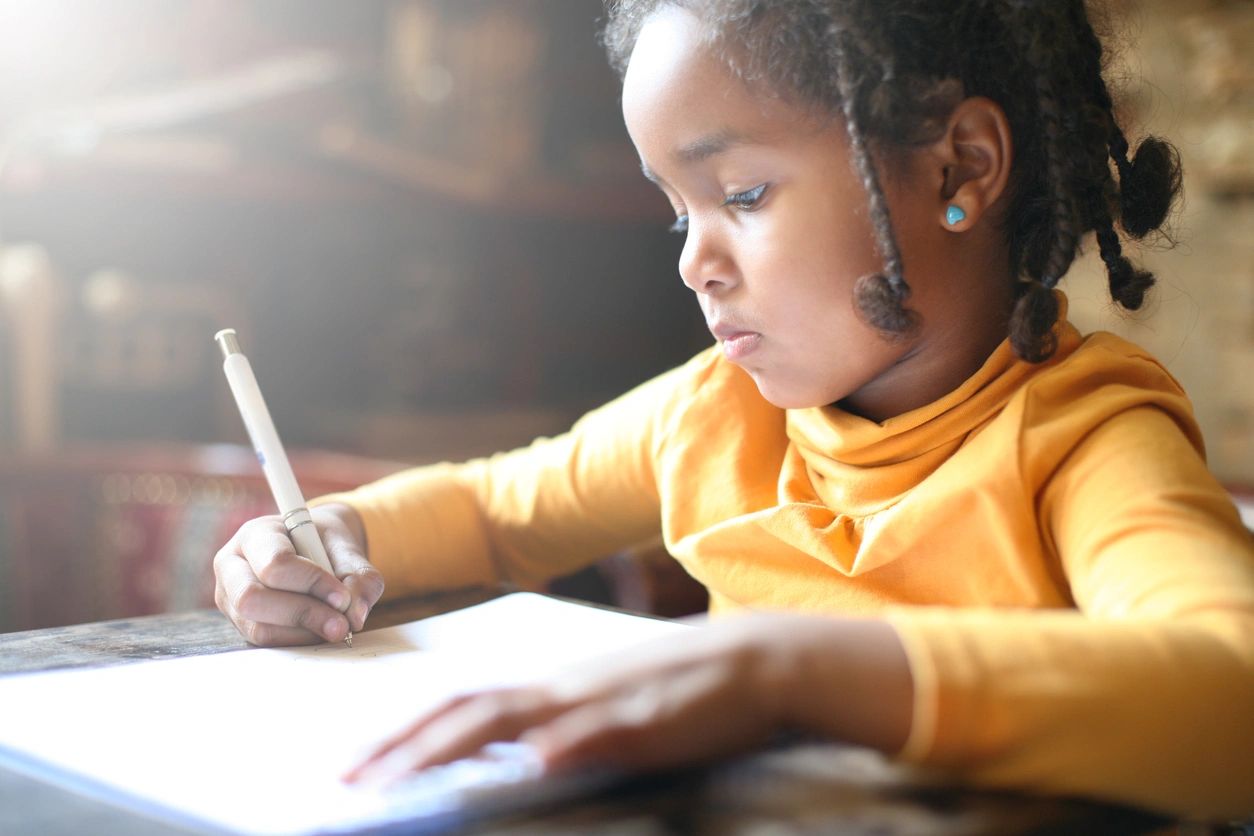A young girl is writing on paper with a pencil.